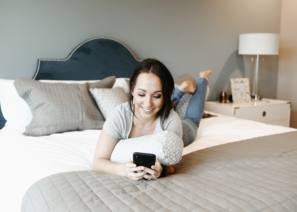 Women laying on her bed and using her phone happily. 